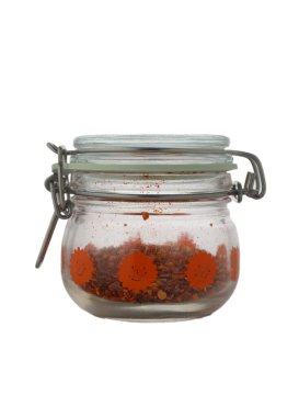 Canlı turuncu çiçeklerle süslenmiş büyüleyici bir cam kavanoz ezilmiş kırmızı biber taneleri içerir, ahşap mutfak tezgahında dinlenir sıcak öğleden sonra ışığında yıkanır, mutfak keşiflerini teşvik eder..