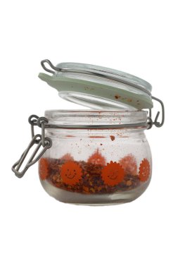 Canlı cam bir kavanoz neşeli bir tasarımla açık durur ve ezilmiş kırmızı biber tanelerinin içeriğini gösterir. Sıcak öğleden sonra güneşi zengin renkleri vurguluyor, mutfak atmosferine sıcaklık katıyor..