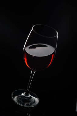 Zengin kırmızı şarapla dolu parlak bir bardak karanlık ve kasvetli bir arka planda duruyor. Yansıyan ışık şarabın derinliğini ve cazibesini ön plana çıkarıyor. Rengi ve inceliğiyle baştan çıkarıcı..