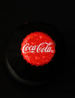 Gaziveren Kıbrıs Rum Kesimi -02.04.2025 Coca Cola Su damlacıklarıyla bezenmiş canlı kırmızı başlık, koyu bir arka planda, yaz eğlencesi ve sıcak toplanmalar sırasında serinletici duygular uyandırarak sahnenin ortasına oturur.