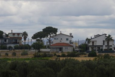 Huzurlu bir sahil köyüne yerleşmiş, bulutlu bir gökyüzünün altında, yemyeşil ve uzak tepelerle çevrili, huzurlu, sakin bir atmosferi somutlaştıran, tuhaf evler duruyor..