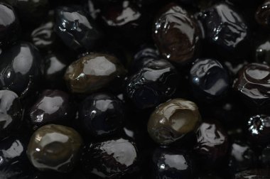Parlak siyah zeytinler birbirine yakın dinleniyor, zengin bir toprak tonunda ışığı yansıtıyor. Yerel meyve bahçelerinden elde edilen ürünler, doğanın kullanılmaya hazır mutfak hazinelerini sembolize ediyor..
