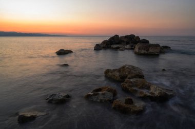 Alacakaranlık sakin sahil şeridine inerken yumuşak renkler gökyüzünde karışıyor. Dalgalar toplanan taşlara çarpar, huzurlu bir rahatlama ve güzellik anı yaratır..