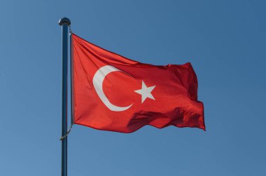 Beyaz hilal ile süslenmiş canlı bir kırmızı bayrak ve hafif esintide gururla dalgalanan bir yıldız. Açık gökyüzü, güzel bir günde çarpıcı bir kontrastı yaratan kalın renkleri yükseltir..