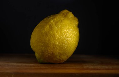 Canlı bir limon, rengini ve dokusunu aydınlatan nazik ışıkla aydınlatılmış kırsal ahşap bir masada oturur..