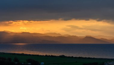 Altın ışık ufukta süzülür, sakin suyu aydınlatır ve dönen dağlara gölge düşürür. Bu resim gibi an, doğanın çarpıcı güzelliğini şafakta yakalar..