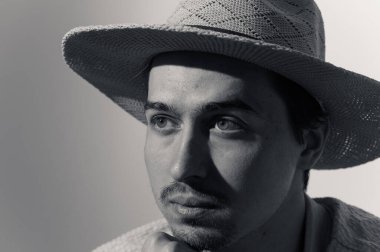 Genç bir adam zarif bir örgü şapka takmış, düşünceli bir şekilde bakıyor. Yüzünde yumuşak gölgeler belirdi, içsel gözlem ve yaratıcılık atmosferi yarattı, anlamlı özelliklerini vurguladı..