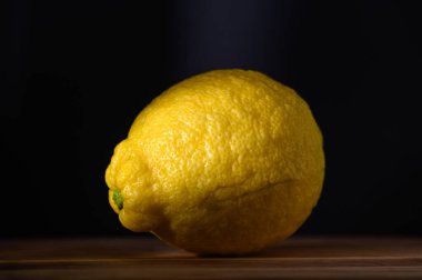 Canlı bir limon, ahşap üzerinde dinlenen loş bir ortamda hafifçe aydınlatılmış dokusu ile göze çarpar..