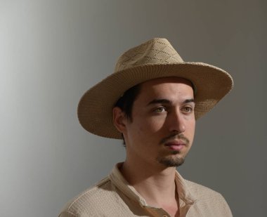 Genç bir adam kendine güvenerek duruyor, özel bir yetenek katan hasır bir şapka takıyor. Düşünceli bakışları, kişiliğini ve karakterini ön plana çıkaran sessiz bir yansıma anı yakalıyor..