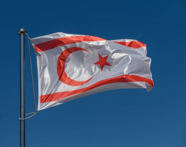 Kuzey Kıbrıs 'ın canlı bayrağı açık mavi gökyüzüne karşı dalgalanıyor. Beyaz arka planda, kültürel gurur ve birliği temsil eden, çarpıcı bir hilal ve yıldız tasarımı sergiliyor..