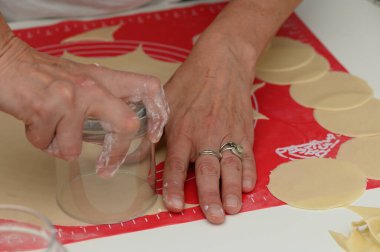 Eller, bir fırın projesi için kusursuz yuvarlak şekiller kesmek için cam kullanarak, parlak bir yüzeye ustalıkla hamur döker. Atmosfer sıcak ve davetkar. Mutfak yaratıcılığı için mükemmel..