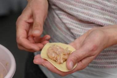 Doğal ışıkla yıkanmış sıcak bir mutfakta, eller makarnaları ustalıkla birleştiriyor, ince makarna tabaklarına baharatlı dolgu yapıyor, ev yapımı mutfak sanatını vurguluyor..