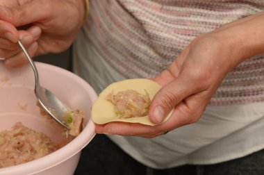 Yetenekli bir aşçı ince hamur ambalajını lezzetli et ve sebze karışımıyla dikkatlice doldurur. Mutfağın sıcacık parıltısı yemek pişirme ritüeline biraz ahmaklık katıyor..