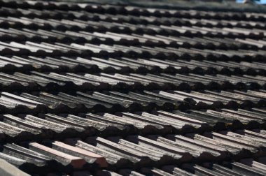 Güneş ışığı, huzurlu bir köydeki geleneksel çatı kiremitlerinin dokulu yüzeyinden yansıyarak işçiliği ve zamansız tasarımı vurguluyor. Doğa ve mimari yukarıda uyum içinde harmanlanır..