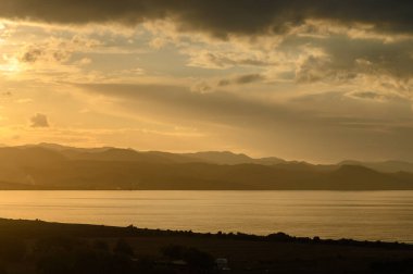 Gün batımında sakin sularda altın ışık dans eder, nefes kesen bir sükunet ortamında tepeleri aydınlatır..