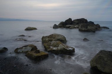 Alacakaranlık çöktüğünde, dalgalar kıyı boyunca uzanan engebeli kayaları okşayarak rahatlatıcı bir melodi yaratır. Sessiz gökyüzü sakin kıyı manzarasına bir sükunet hissi yansıtır..