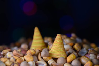 Parlak renkli konik ikramlar çeşitli fındık ve tohumlardan oluşan bir yatağın üzerinde dinleniyor ve neşeli bir görüntü yaratıyor. Işıkların yumuşak parıltısı bu neşeli mutfak düzenine canlı bir ortam ekler..