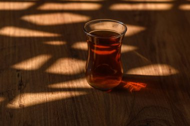 Yumuşak gün ışığıyla güzelce aydınlatılmış, kırsal ahşap bir masanın üzerinde narin bir bardak çay duruyor..