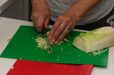 Basit bir mutfak düzeniyle çevrili canlı yeşil bir kesme tahtasının üzerinde ustalıkla taze lahana dilimler. Akşam yemeği hazırlıkları başlarken taze sebzelerin kokusu havayı dolduruyor..