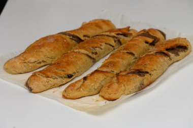 Üç uzun, kabuklu ekmek somunu parşömenin üzerinde duruyor, altın-kahverengi dış görünüşleri lezzetli, sıcak bir iç mekanı işaret ediyor. Mutfak dekoru çok parlak, mutfak yaratıcılığına davetiye çıkarıyor..