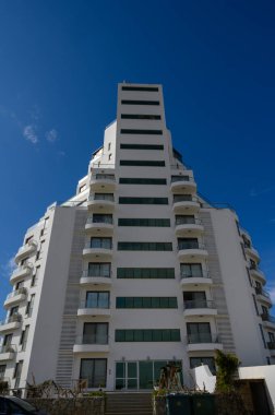 Çarpıcı bir çağdaş bina, eşsiz tasarımı ve güneş ışığını yansıtan geniş pencereleriyle berrak gökyüzüne doğru yükselir. Yakındaki yeşillik şehir cazibesini artırıyor..