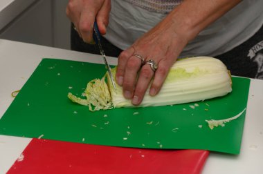 Eller parlak yeşil bir kesme tahtasının üzerinde ustalıkla taze bir lahana kafası dilimler. Mutfak taze malzemelerle dolu sağlıklı bir yemek hazırlamanın mutluluğuyla uğulduyor..