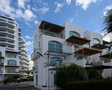 Parlak, havadar binalar altın güneş ışığıyla güneşlenir, mavi gökyüzünün resimli arkaplanı arasında kıyı tasarımı sergilenir..