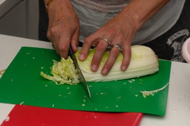 Mutfak enerjisi havayı doldururken, eller yeşil kesme tahtasındaki canlı lahanayı ustalıkla kesiyor. Lezzetli yemekler ve yaratıcılık için taze malzemeler hazır..
