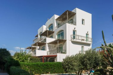 Balkonları olan çarpıcı bir bina, açık mavi gökyüzünün altında yeşil bitkilerle çevrili çarpıcı manzaralar sunuyor..