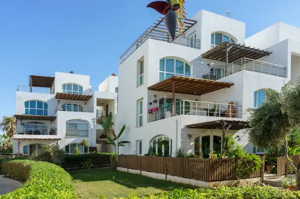 Canlı yeşilliğe sahip modern binalar açık mavi gökyüzünün altında sahil kenarında sakin bir ortam yaratıyor..