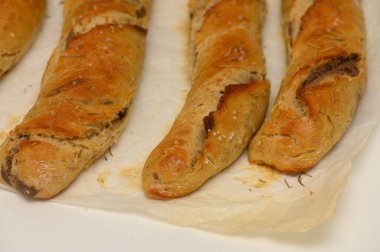 Parşömen kağıdına üç uzun, taze pişmiş ve altın-kahverengi kabuklu ekmek konservesi yerleştirilir. Dokuları davetkar, biberiye dalları, sıcaklığı ve ev yapımı konforu çağrıştırıyor..