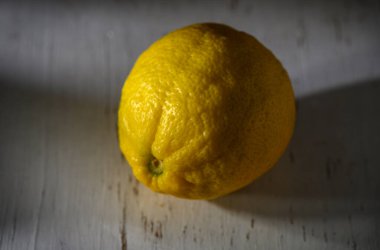 Canlı bir limon, dokulu bir yüzeyde oturur. Günün yumuşak ışığında tazelik ve sadelik yayar..