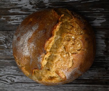 Sıcak, kabuklu bir somun ekmek ahşap bir masanın üzerinde duruyor, altın kabuğunu ve havasını sergiliyor..