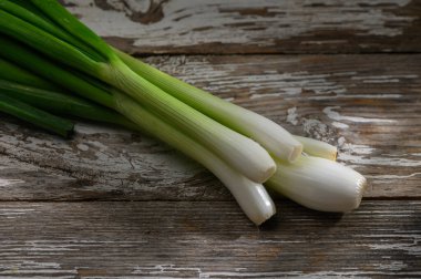 Canlı yeşil soğanlar yıpranmış ahşabın üzerinde dinleniyor, taze görünüşlerini ve yemek pişirmek için çekici dokularını sergiliyorlar..