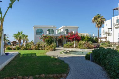 Lüks villa, tropikal bitkilerin ve çiçek açan çiçeklerin arasında, göz kamaştırıcı bir sahil manzarasına bakıyor..