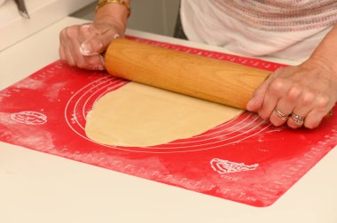 Bir çift el hamur işini parlak, desenli bir hasırın üzerine serer ve pişirme zevkleri için mükemmel bir temel oluşturur..