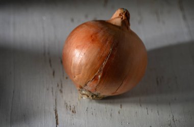 Kahverengi bir soğan yıpranmış ahşap bir yüzeyde oturur. Yüzeyi yumuşak doğal ışığı yansıtır ve çatlaklarını aydınlatır..