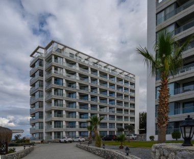 Geniş pencereli, palmiye ağaçları ve dramatik bulut örtüsüyle çerçevelenmiş çok katlı etkileyici bir bina..