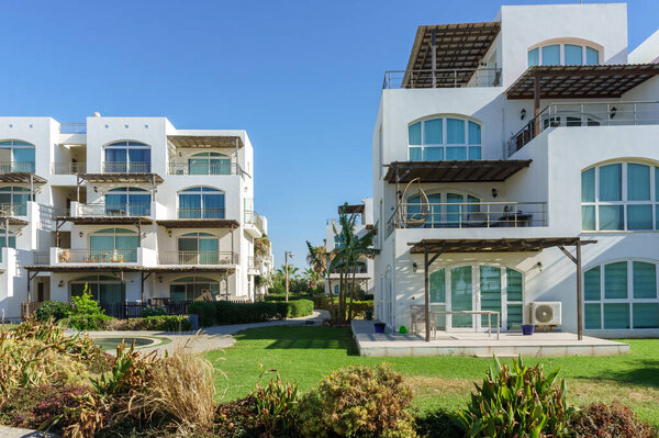 Стильные белые виллы изящно стоят перед ярким голубым небом, окруженные зелеными пейзажами..