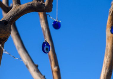 Geleneksel olarak negatif enerjiden koruduğuna inanılan renkli mavi tılsımlar kırsal bir ağaçtan açık mavi gökyüzü zeminine doğru zarif bir şekilde sarkmaktadır. Sanat ve doğa güzel bir şekilde birleşir..