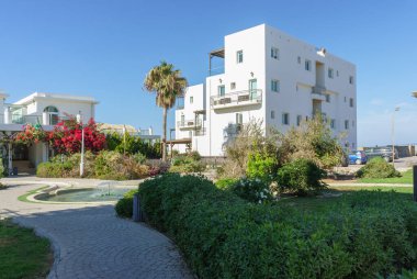 Parlak bahçelerle çevrili çarpıcı beyaz binalar deniz kenarında sakin bir atmosfer yaratıyor..