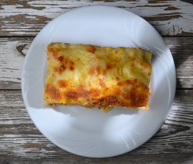 Cazip bir lazanya servisi basit beyaz bir tabakta, makarna katmanları, zengin sos ve erimiş peynir sergileniyor. Bu doyurucu yemek hafta sonu buluşması için mükemmel..