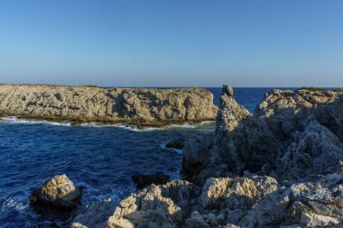 Dalgalar yavaşça engebeli bir kıyı şeridine çarpar, sıcak altın ışıkla yıkanır akşama geçiş gibi..