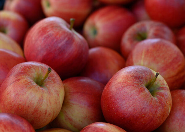 Ярко-красные яблоки сложены вместе, блестя на солнечном свете на оживленном фермерском рынке. Атмосфера отражает очарование осени яркими красками и живой болтовней.