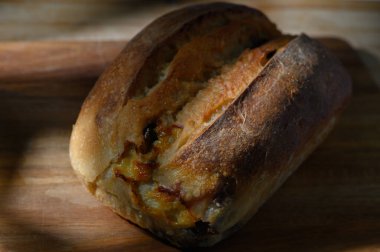 Altın kabuklu somun, yumuşak gölgelerle çevrili kırsal ahşap bir yüzeye davetkar bir şekilde yerleştirilmiş karamelize edilmiş kenarları gösterir..