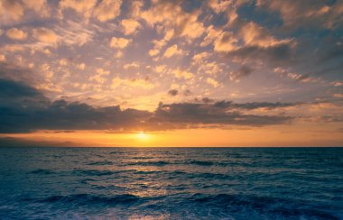 Altın güneş ışığı ufukta süzülür. Hafif dalgalar alacakaranlıkta kıyıya vurur. Huzurlu bir atmosfer yaratır..