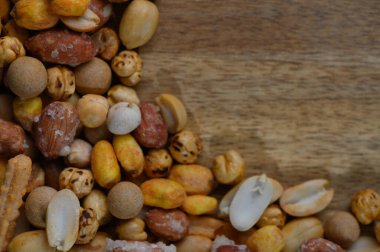 Kavrulmuş fındık ve abur cuburlardan oluşan canlı bir çeşitlilik kırsal ahşap bir yüzeyde mevcuttur, çeşitli şekil ve renkler sergilenmektedir, daha yakından bakmaya davet edilir ve enfes bir tatma deneyimi.