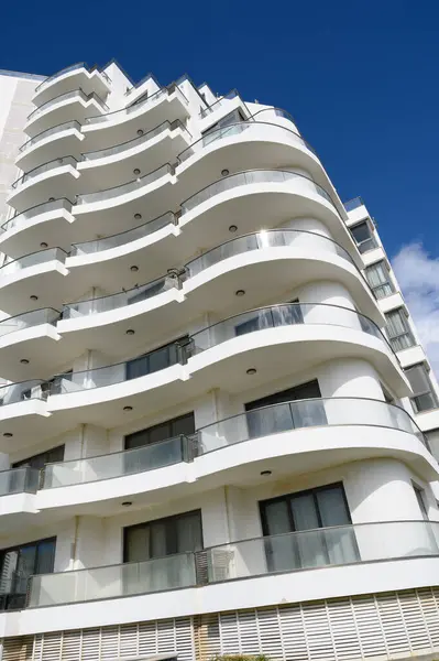 Çarpıcı bir bina, güneşli bir günde çağdaş mimari güzelliği ön plana çıkaran açık mavi gökyüzüne karşı parlak bir cephe ve akan balkonlara sahiptir..