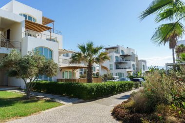 Bereketli yeşillik, berrak mavi gökyüzünün altındaki zarif villalara giden kaldırım taşı yolu çiziyor..