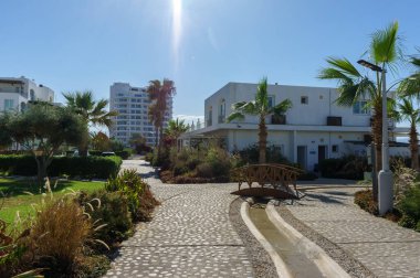 Huzurlu bir yol modern evlerin ve bereketli palmiye ağaçlarının yanından geçiyor, güneşin altında sakin yürüyüşlere davet ediyor..